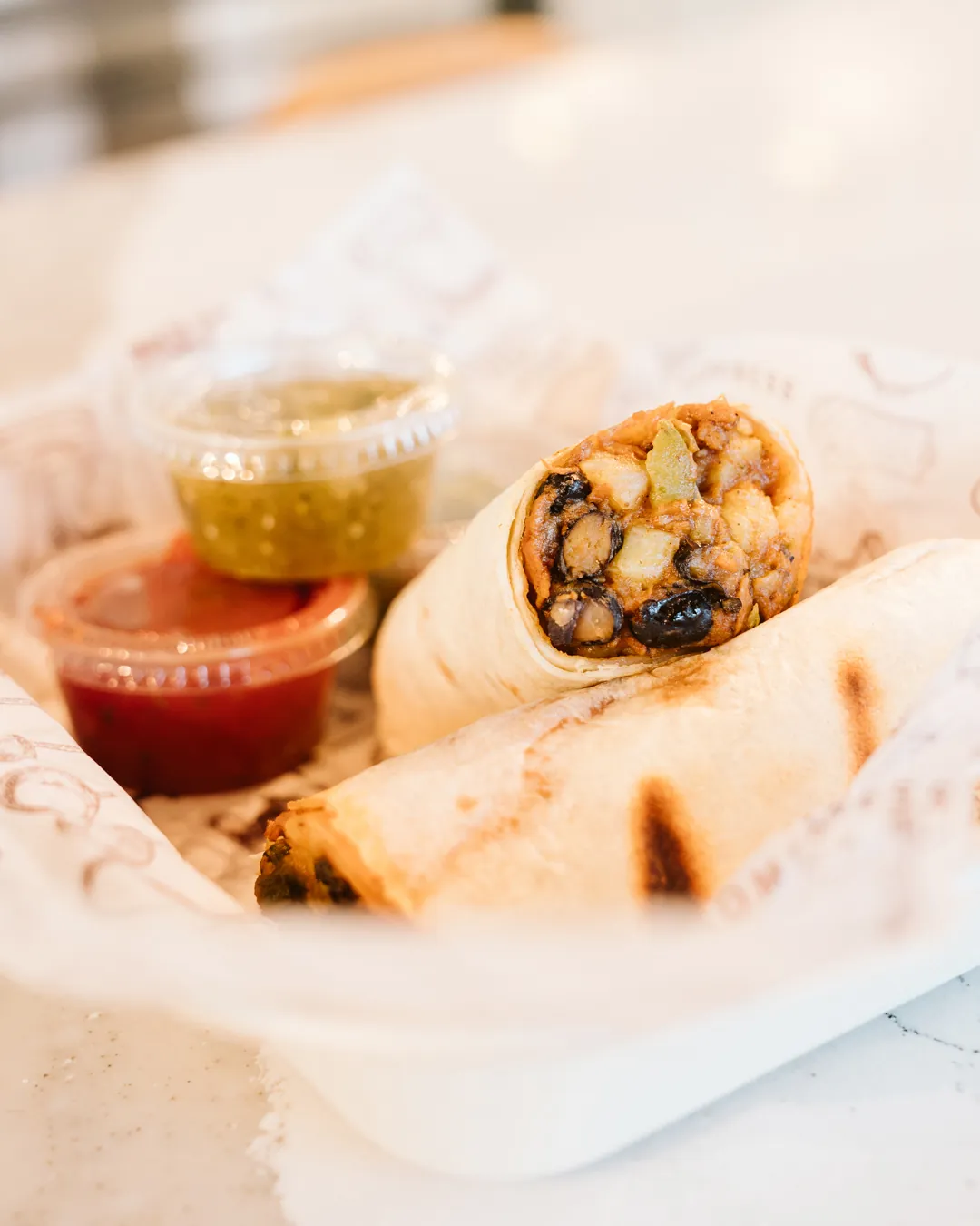 Breakfast burrito cut open beside red and green salsa