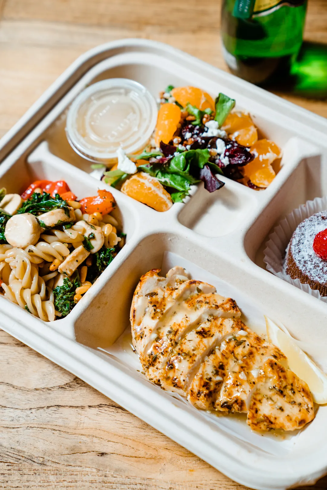 Compartmented takeout meal with chicken, vegetables, salad, and sauce