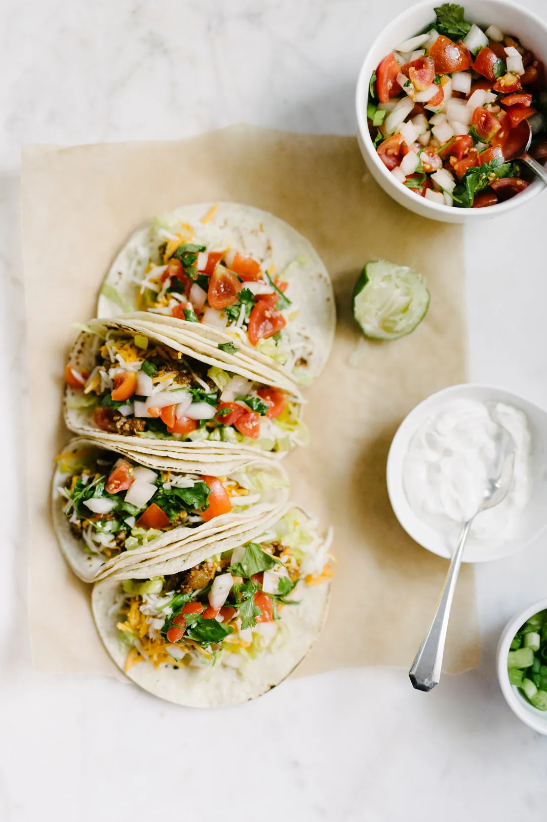 Three tacos with tomato salsa, guacamole, and sour cream