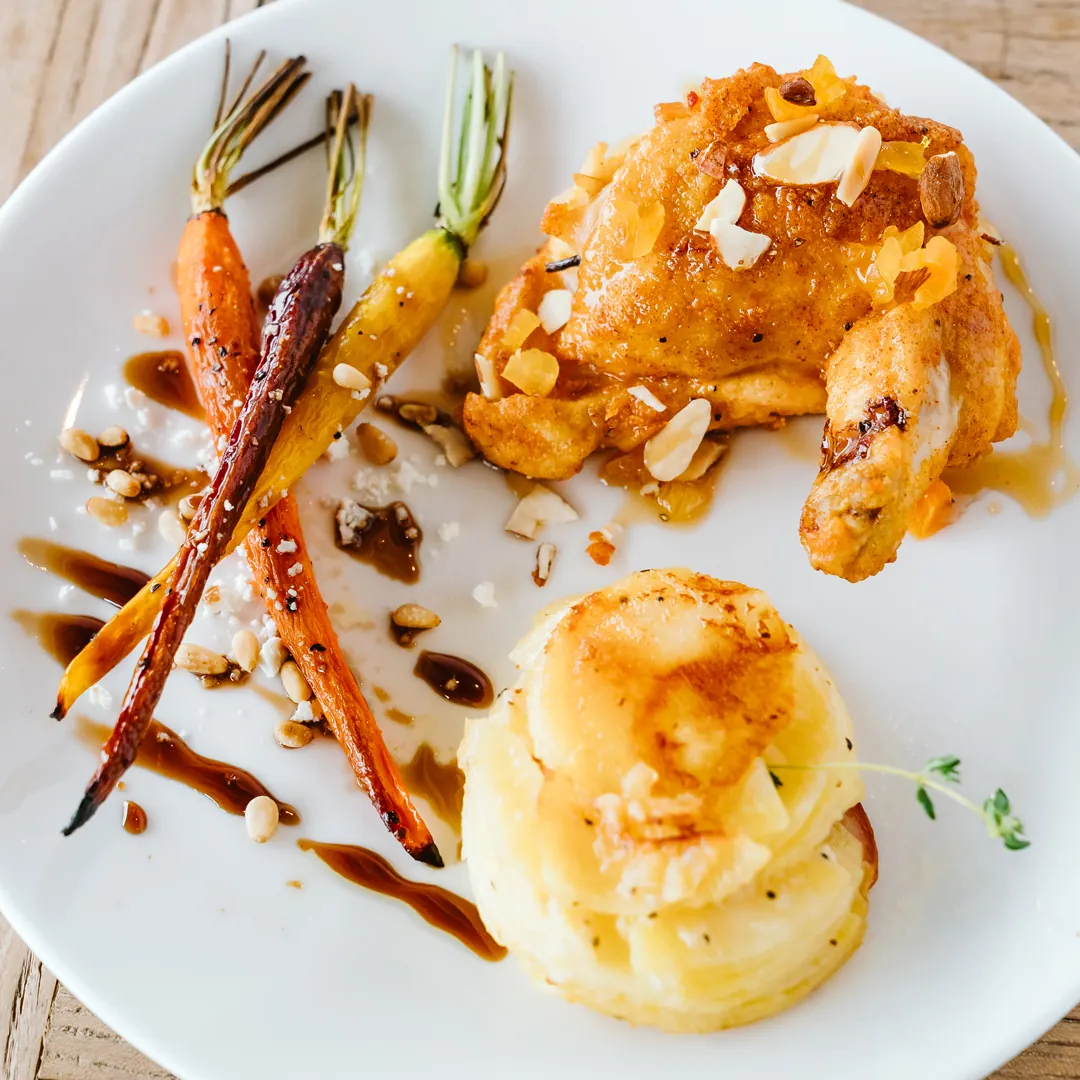 Plated chicken with rainbow carrots and a layered potato side