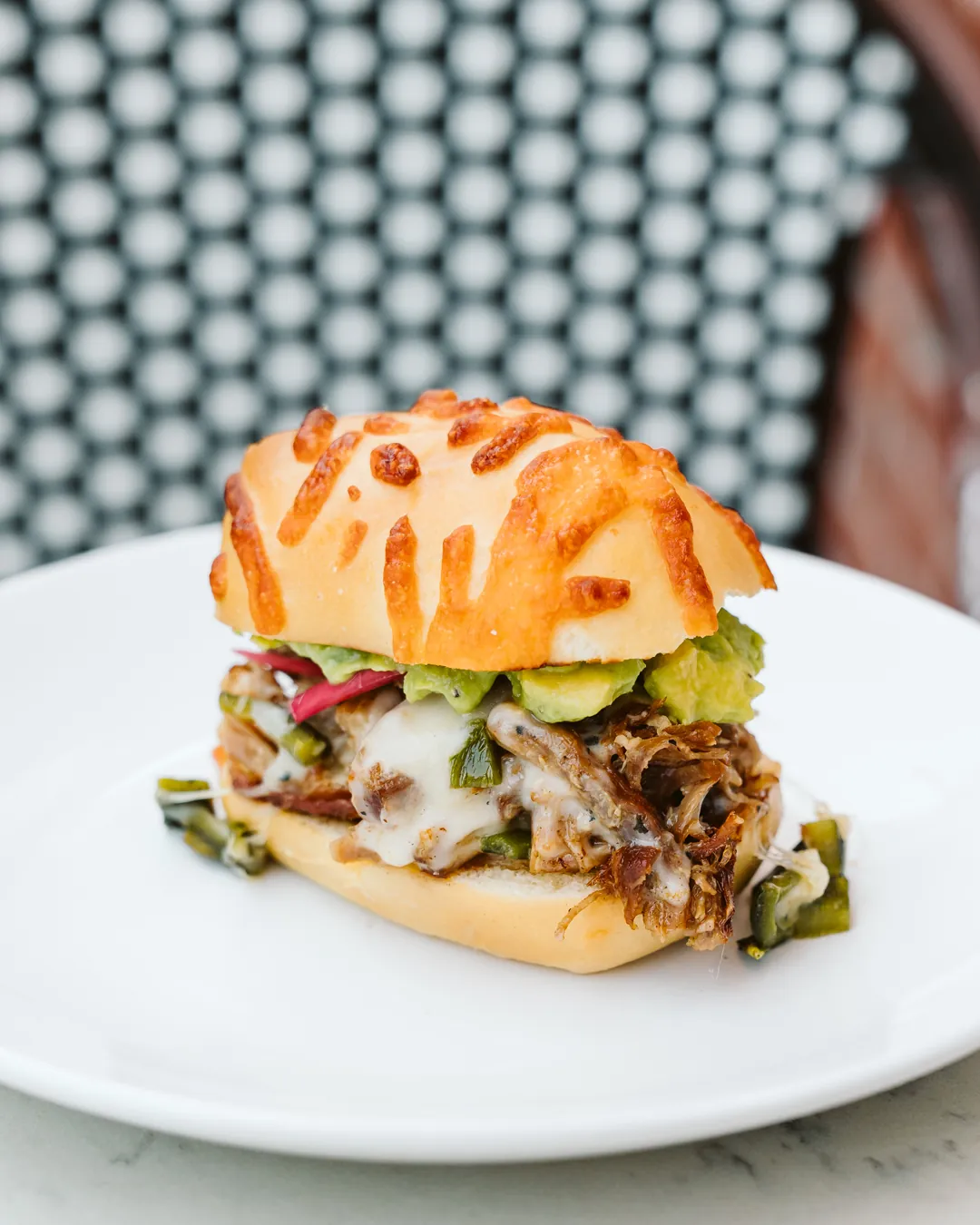 Carnitas slider with provolone, roasted peppers, avocado, and pickled onion