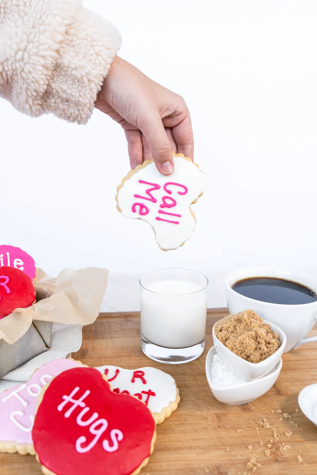 Hand placing a Call Me conversation heart cookie by decorating supplies
