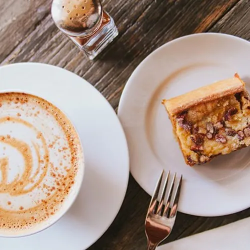 Latte and a pecan dessert bar on a wooden café table