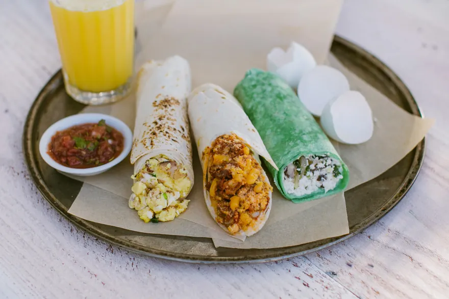 Three breakfast burritos with salsa, orange juice, and decorative eggs