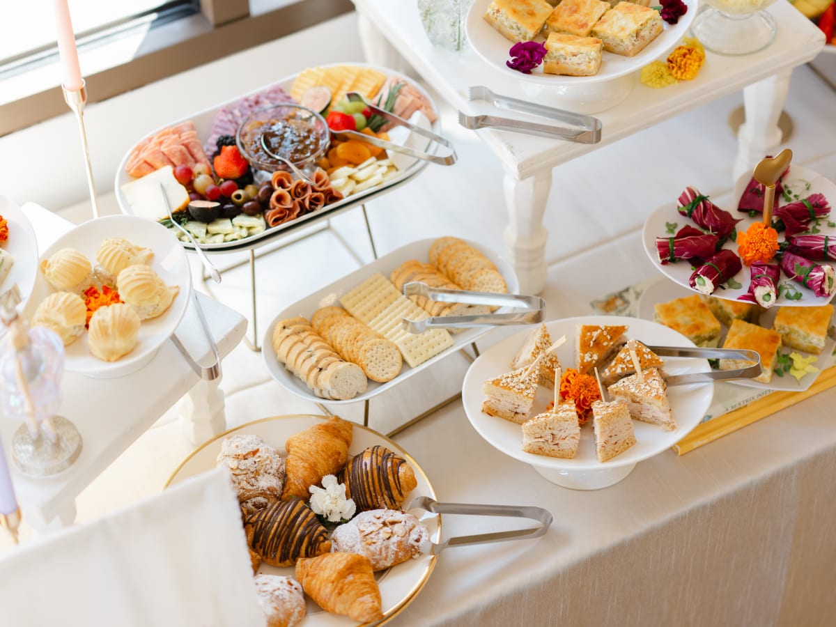 Tea sandwiches, pastries, quiche and a charcuterie tray arranged for a catered gathering.