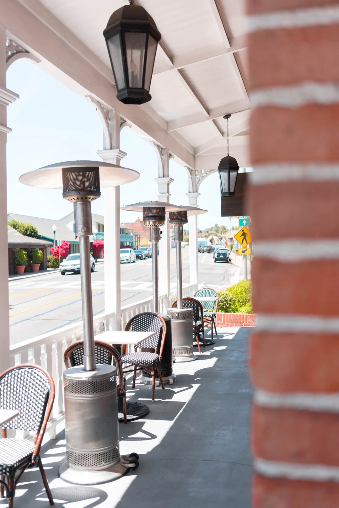 Covered patio with café tables and tall outdoor heaters along a brick wall