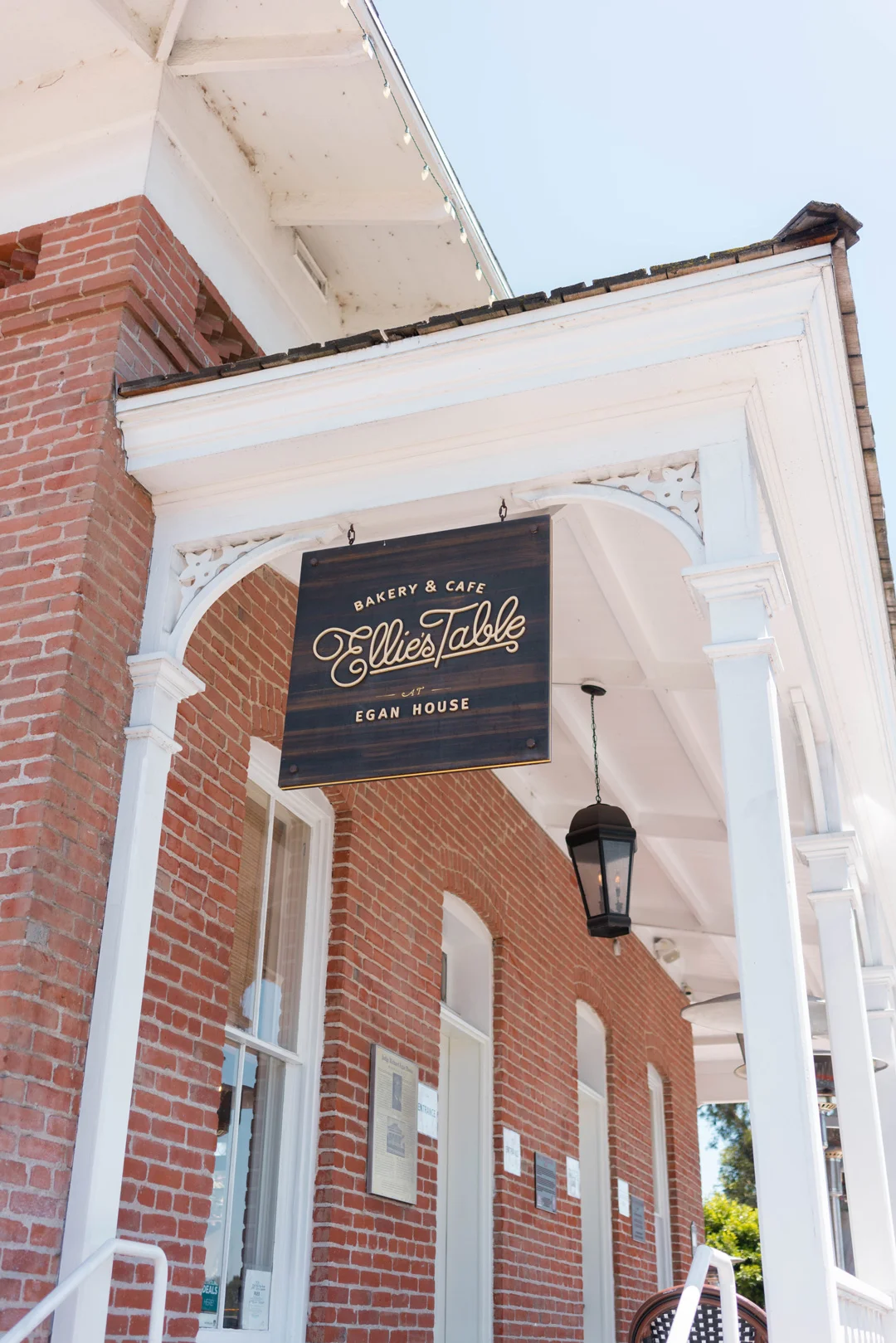Ellie's Table sign mounted beneath the porch roof of the brick building