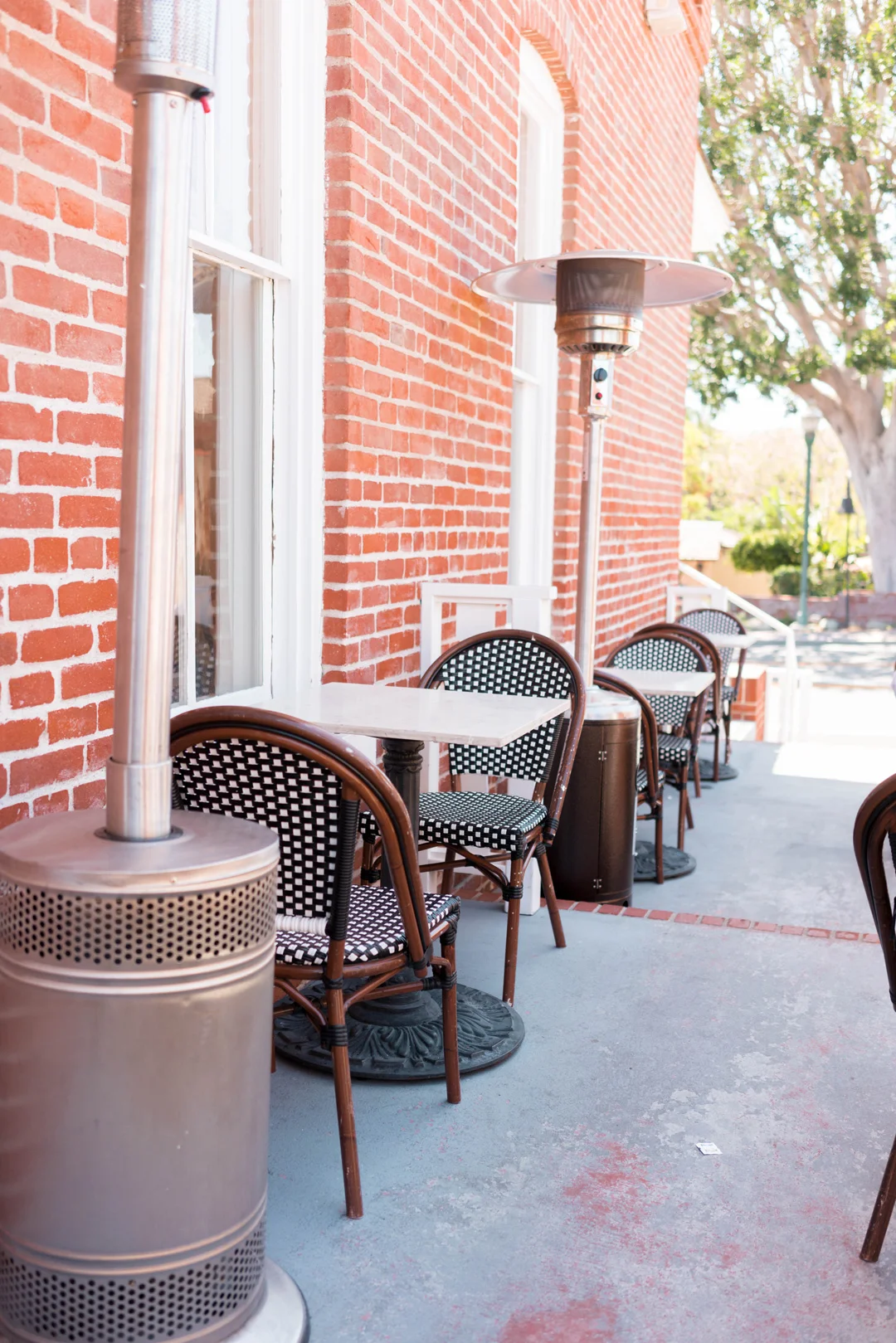Narrow patio beside the brick building with tables and tall heaters