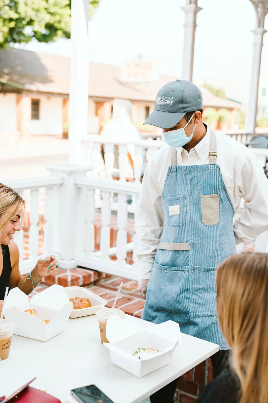 Masked café employee serving diners on the outdoor patio