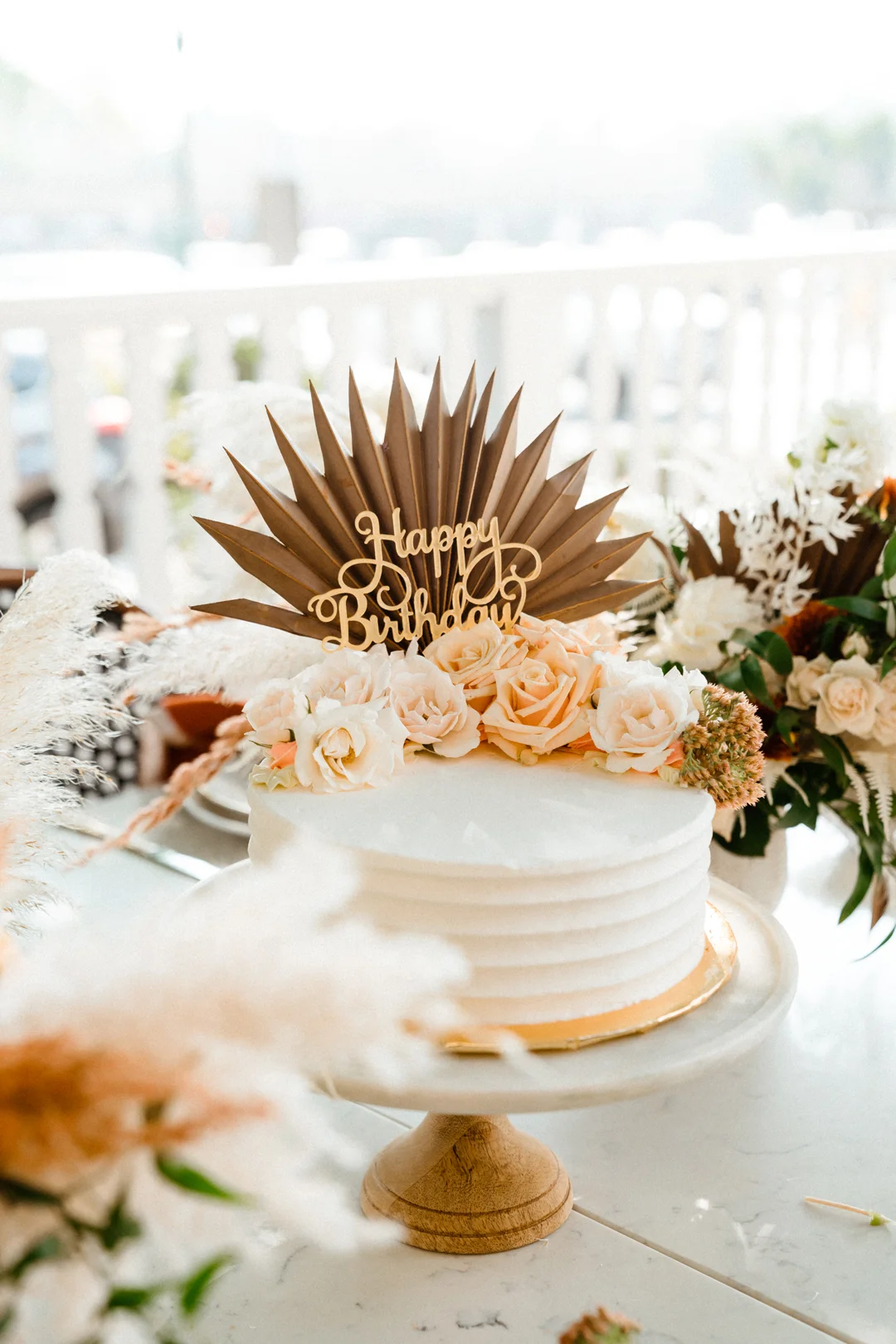 White celebration cake with a wooden topper and pampas grass