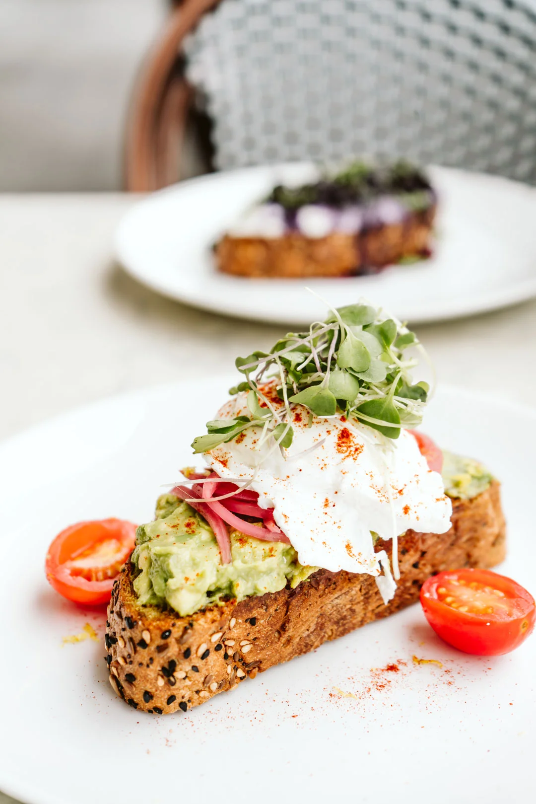 Avocado toast with fried egg and tomatoes on a café table
