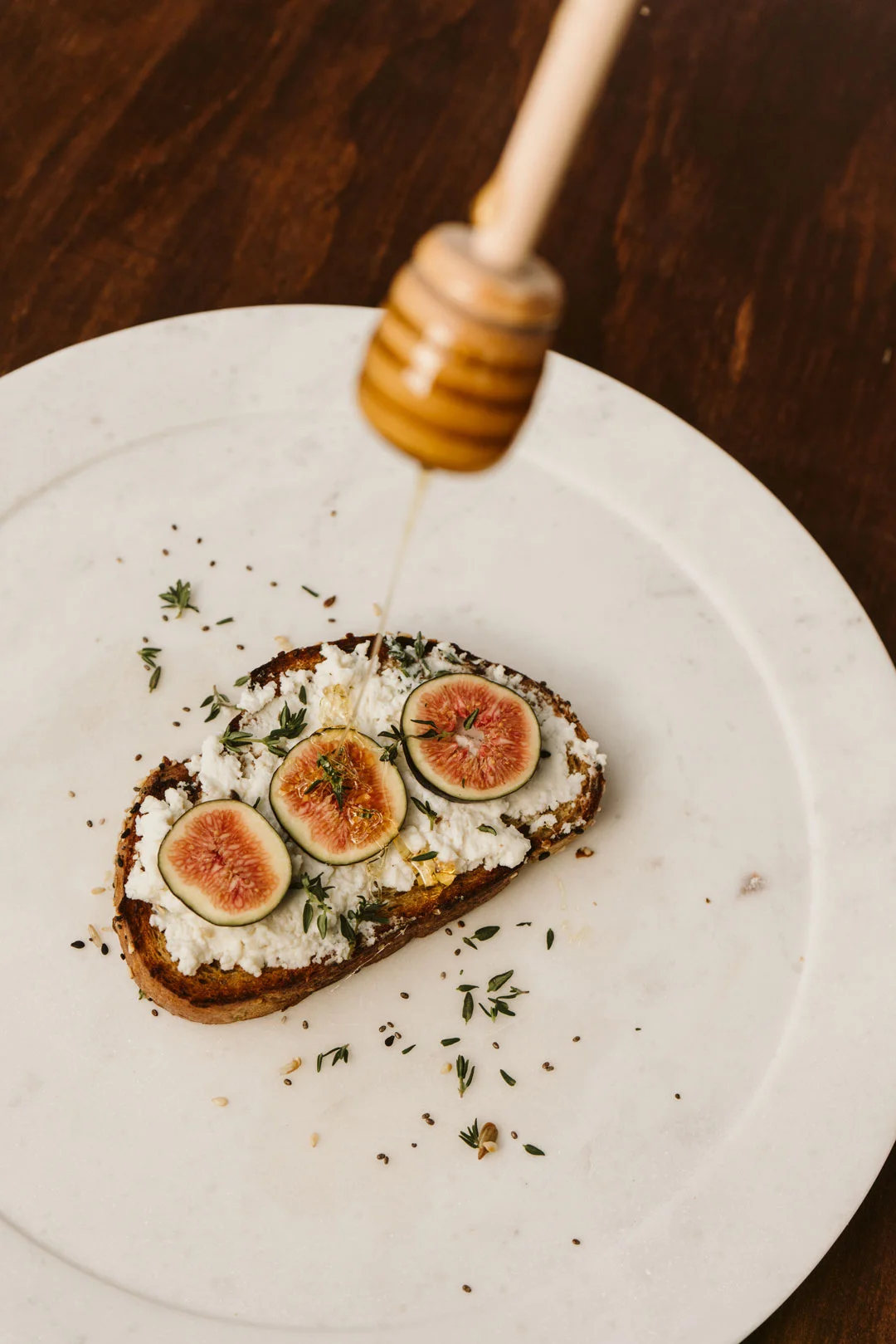 Ricotta toast with sliced figs, thyme, and honey on a white plate
