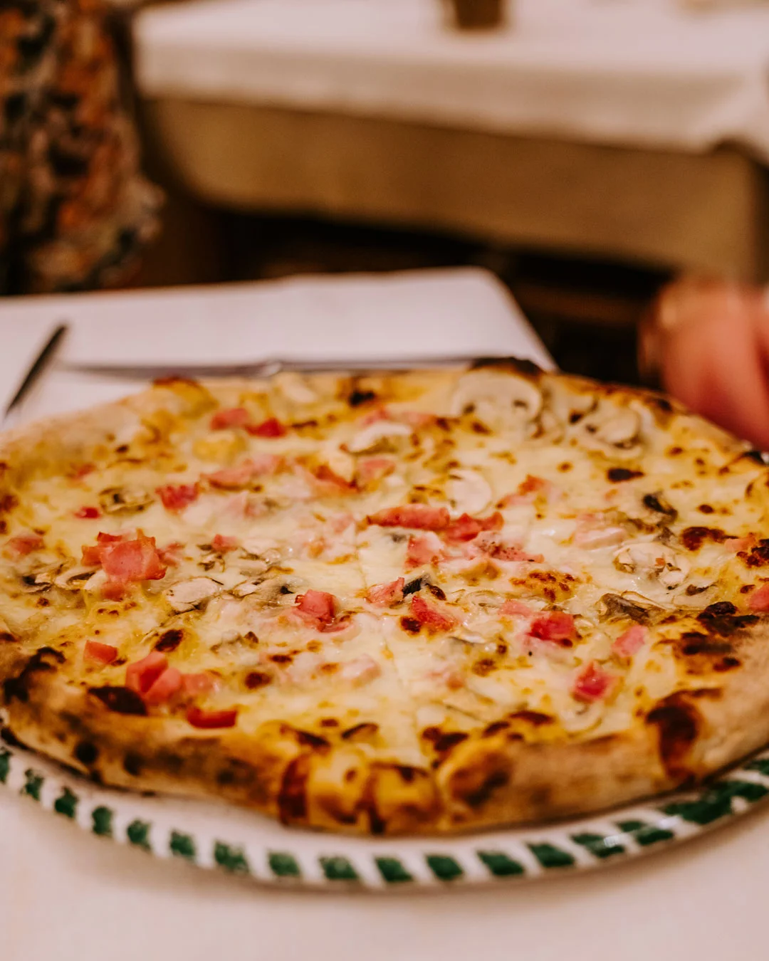 Pizza topped with mushrooms and cured meat on a patterned plate