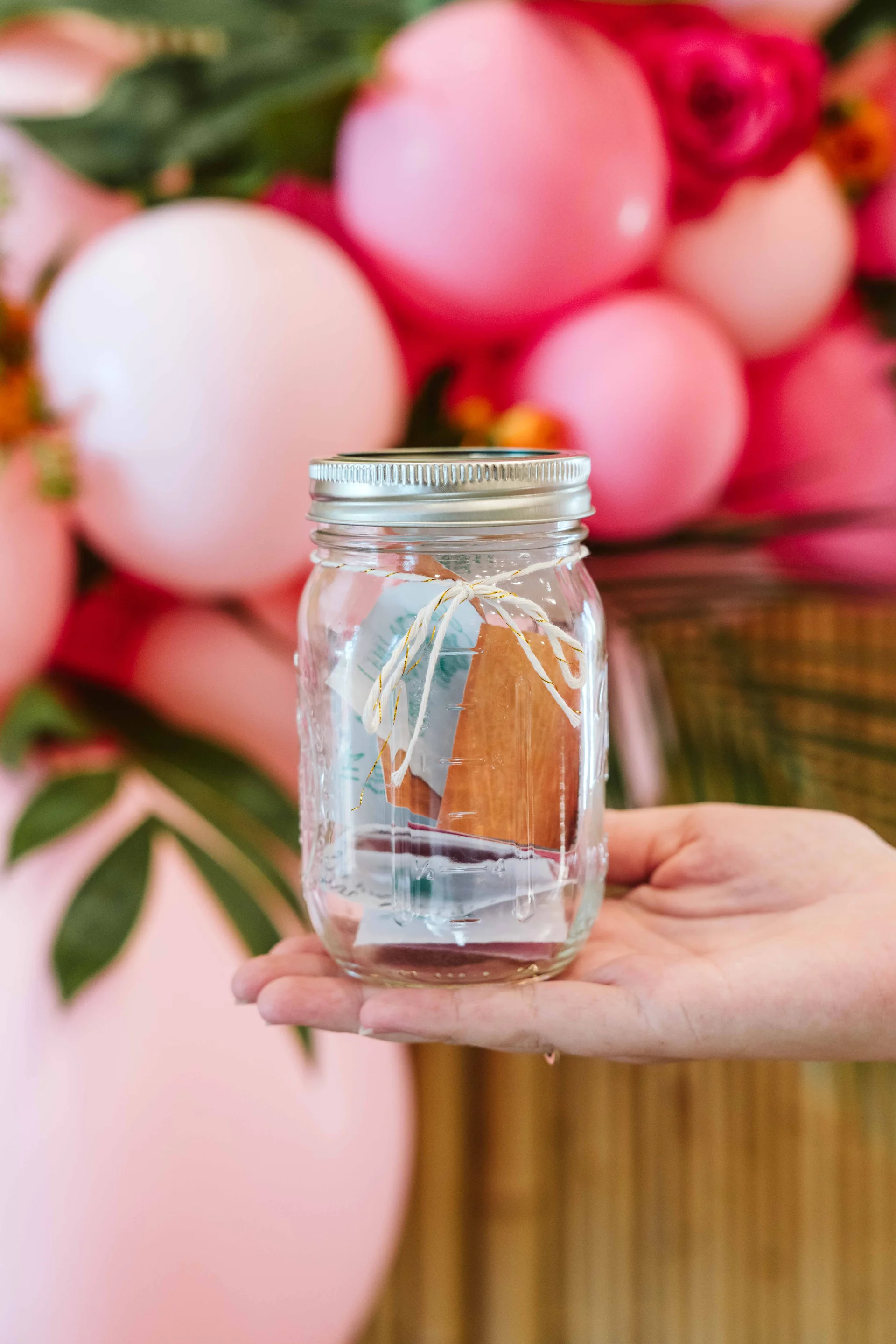 Hand holding an affirmation jar in front of pink balloons