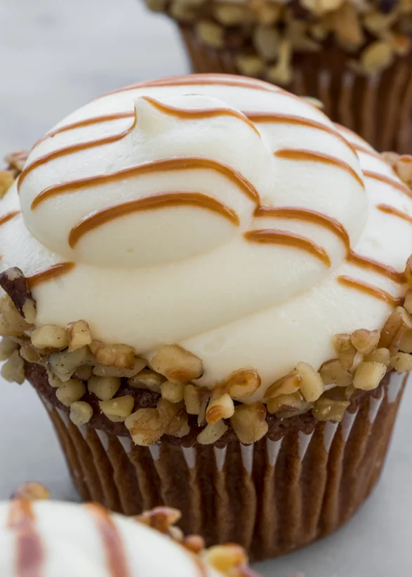 Carrot cake cupcake with cream cheese frosting, caramel drizzle, and chopped nuts