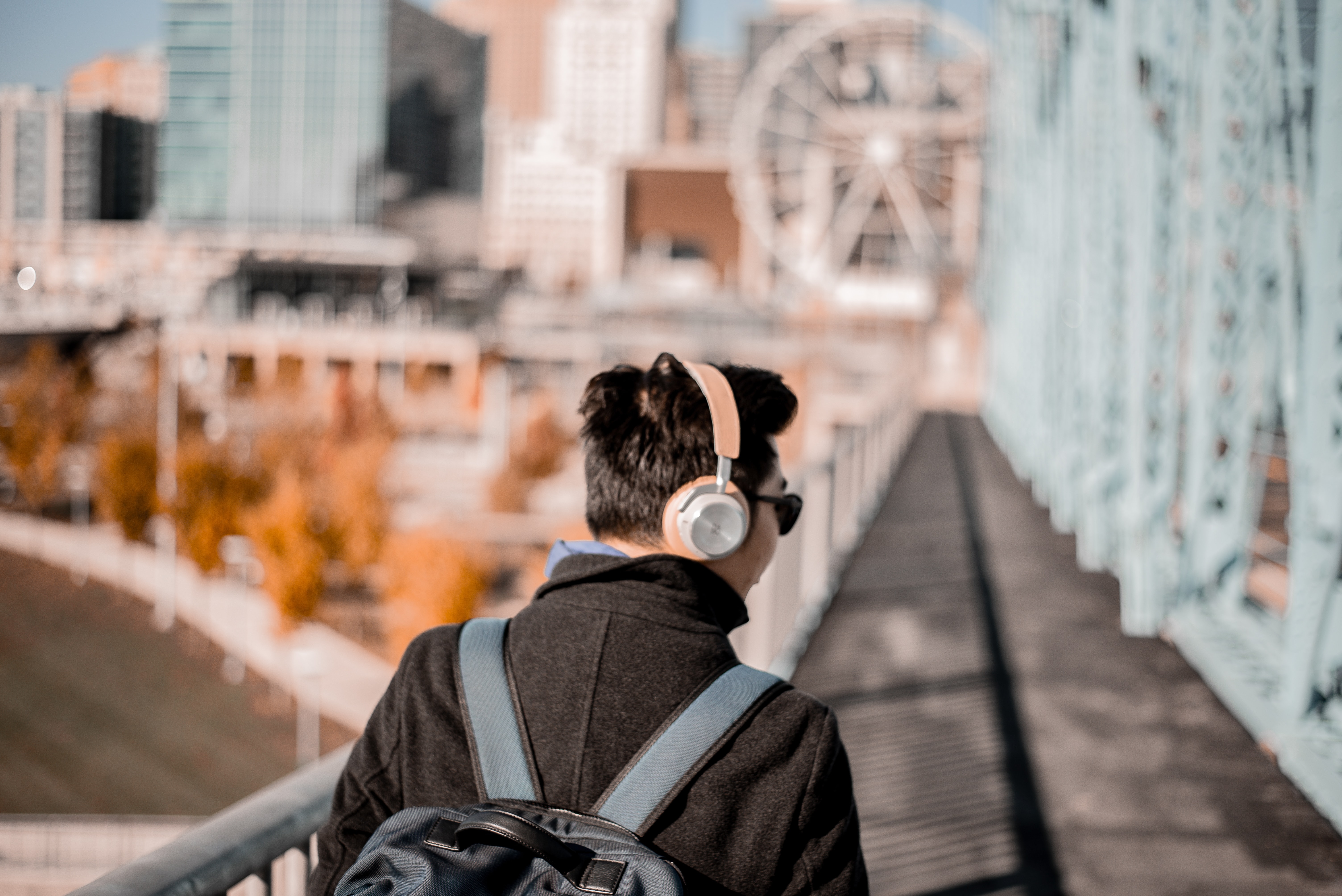 Man with headphones and a backpack walking across bridge.