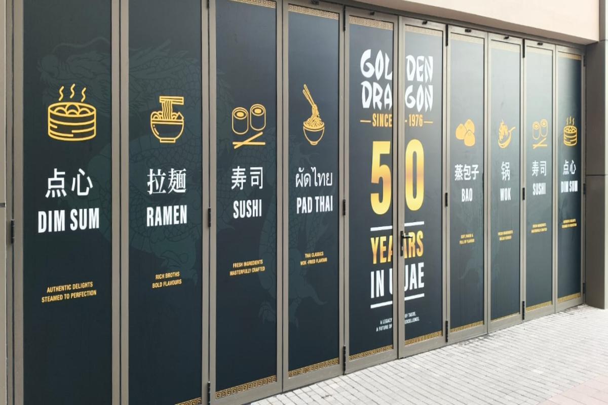 Close-up of Storefront Glass Branding with precise gold iconography for Dim Sum, Ramen, and Sushi applied to black glass panels.