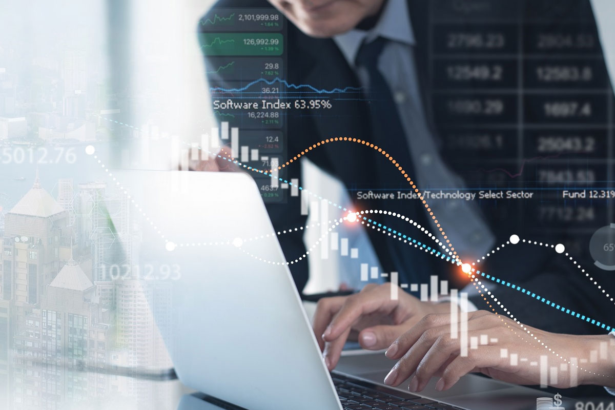A business professional working on a laptop with overlaid digital financial charts and stock market data