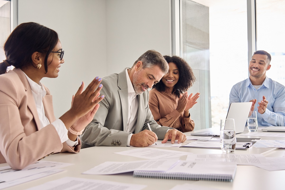 Business team applauding as an executive signs a merger or acquisition agreement during a meeting