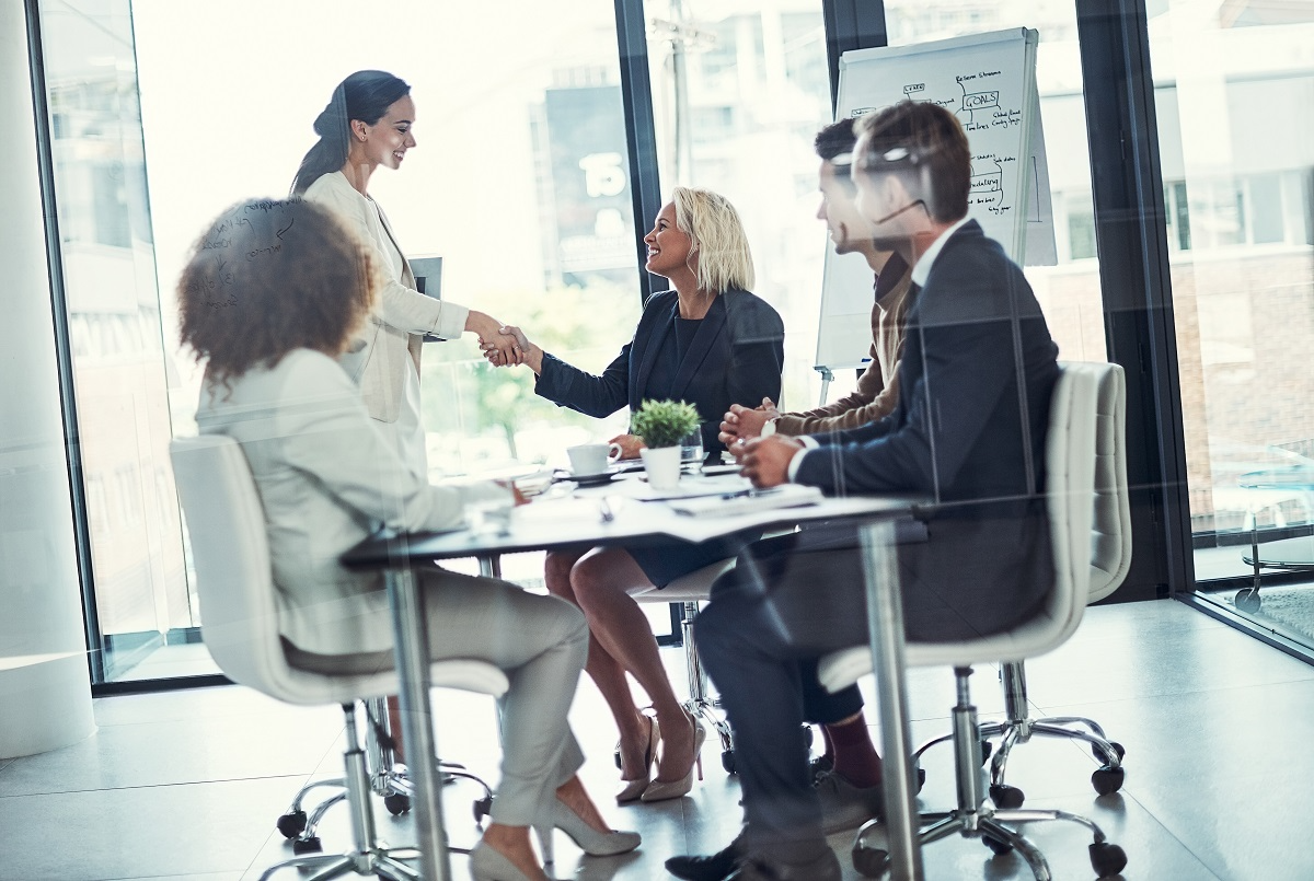 Business executives shaking hands during a corporate meeting in a modern conference room, symbolizing a merger or acquisition agreement and strategic partnership