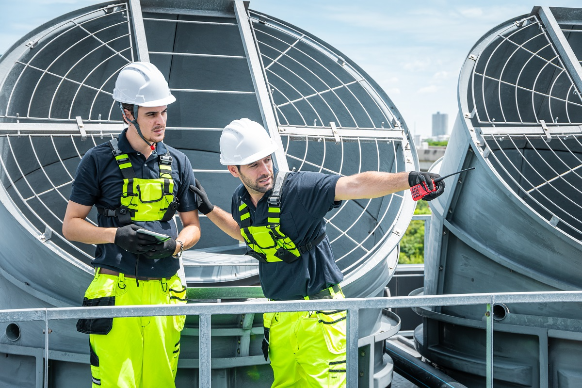 Industrial HVAC technicians wearing safety gear while inspecting and coordinating maintenance on large rooftop ventilation systems