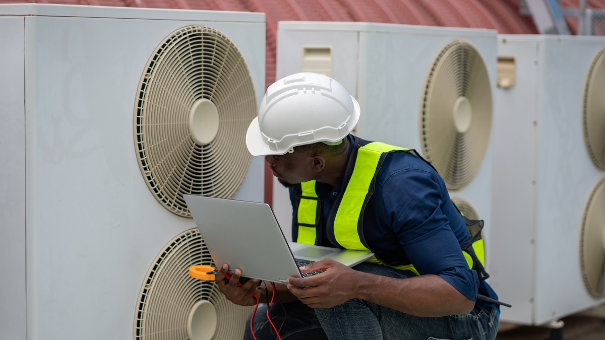HVAC technician using diagnostic tools and a laptop to troubleshoot large commercial air conditioning units