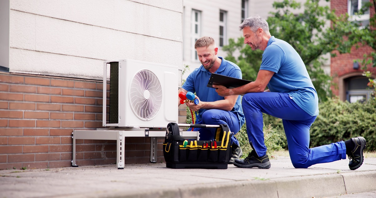 HVAC technicians servicing an outdoor residential air conditioning unit while reviewing maintenance work and equipment performance
