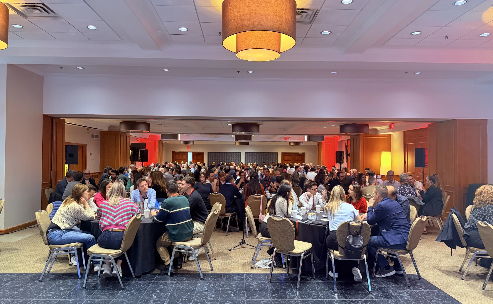 Une grande salle de conférence remplie de participants attablés en rondes, en pleine discussion lors d'un événement.