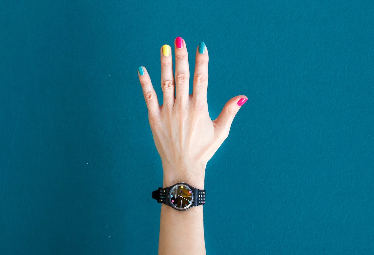 Main aux ongles de couleurs différentes portant une montre.