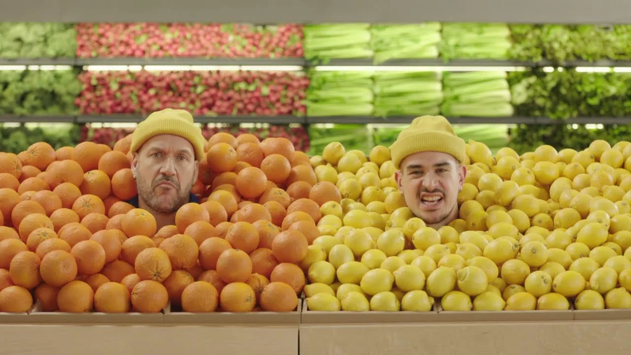 Deux hommes apparaissant au milieu d’un étal d’oranges et de citrons.