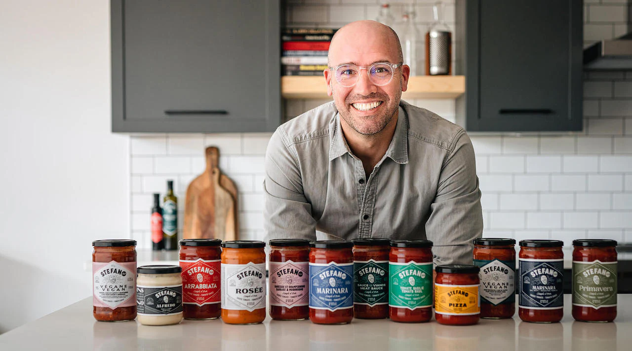 Homme souriant derrière une gamme de sauces en pots.