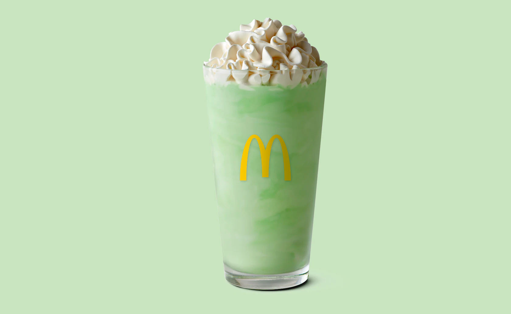 Milkshake vert surmonté de crème dans un verre McDonald’s.