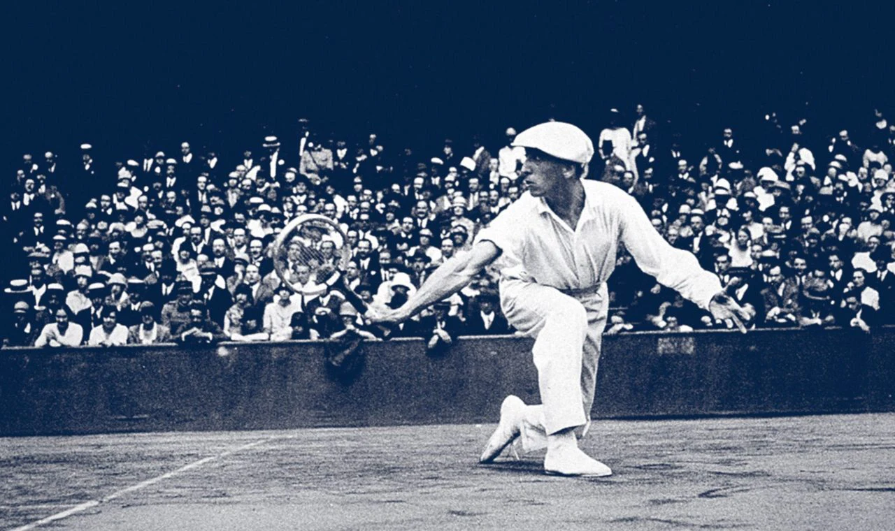 Photographie ancienne d’un joueur de tennis devant les tribunes.