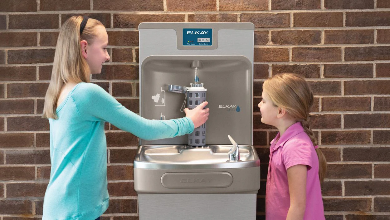 Deux enfants près d’une fontaine permettant de remplir une bouteille d’eau.