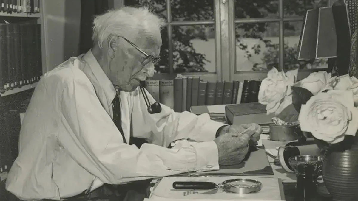 Photographie ancienne d’un homme écrivant à son bureau, une pipe à la bouche.