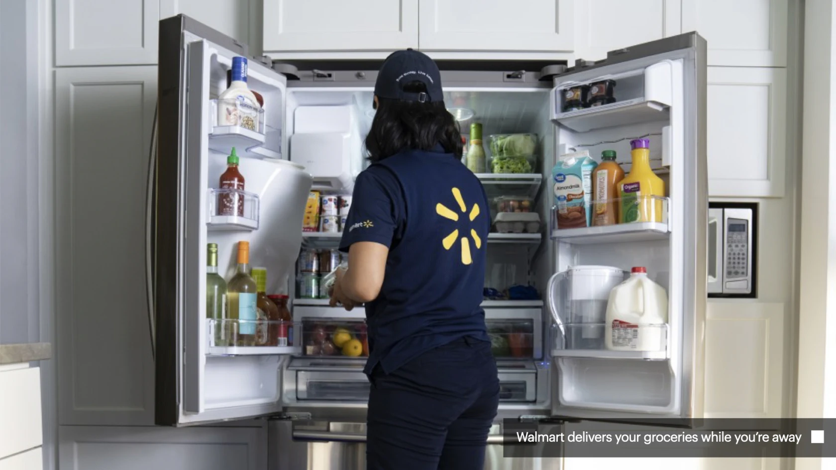 Employée Walmart rangeant des courses dans un réfrigérateur à domicile.