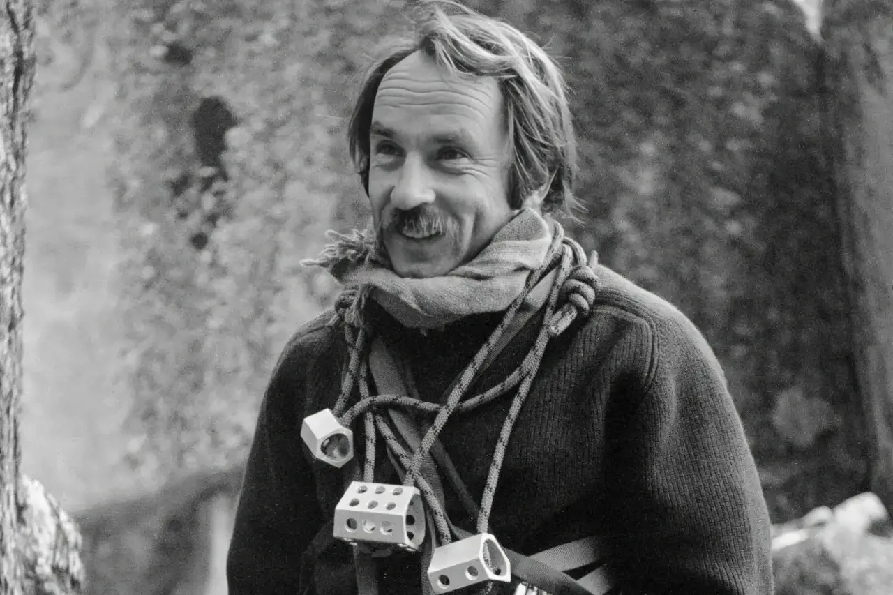 Photographie en noir et blanc d’un alpiniste avec une corde sur l’épaule.