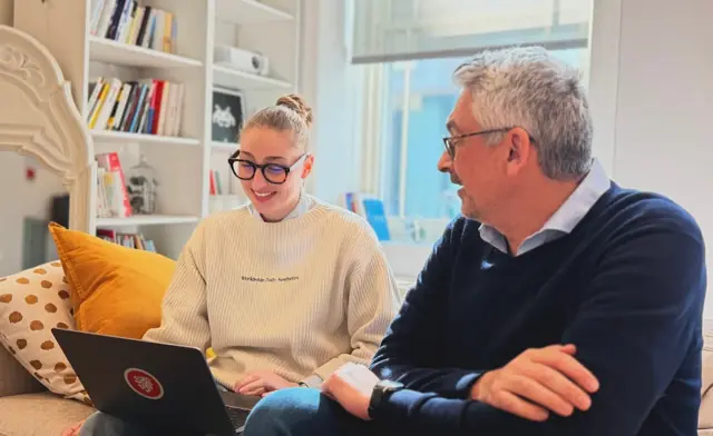 Deux collègues souriants discutent autour d’un ordinateur portable.