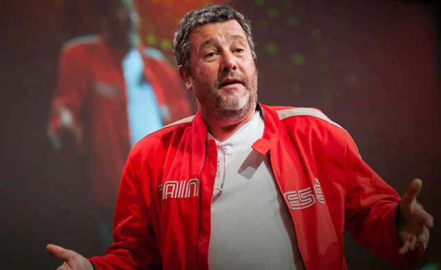 Homme en veste rouge prenant la parole sur scène.