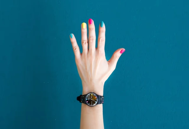 Main aux ongles de couleurs différentes portant une montre.