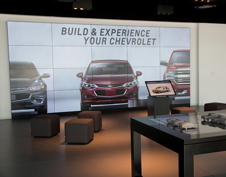 Large video wall with life-size Chevy cars and trucks displayed within dealership
