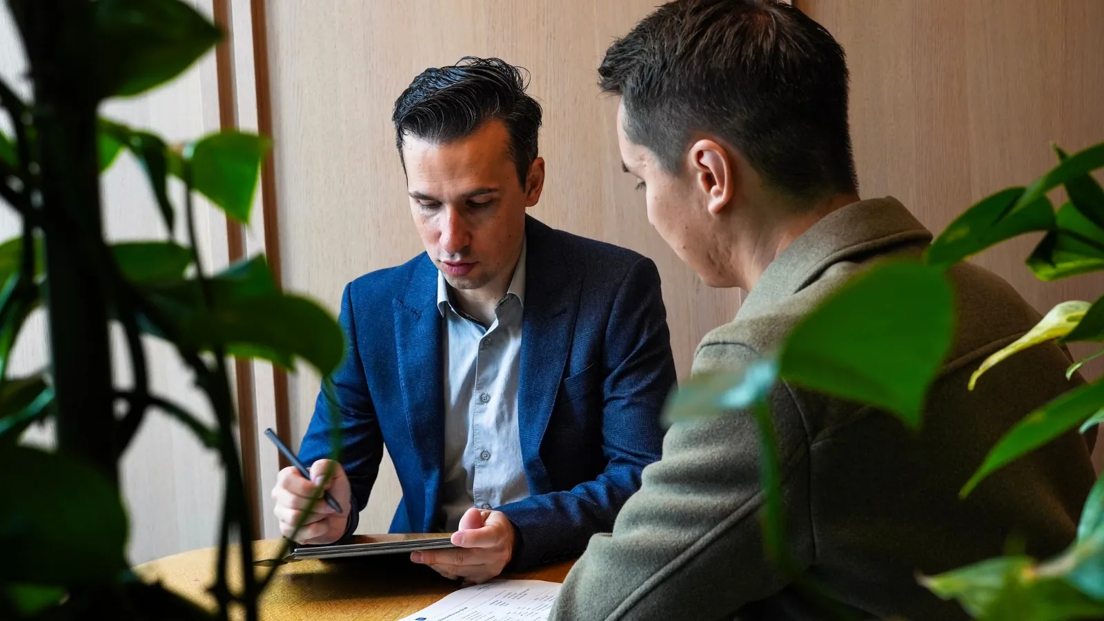 Julien Mainguy writing notes with a client, framed by green plants