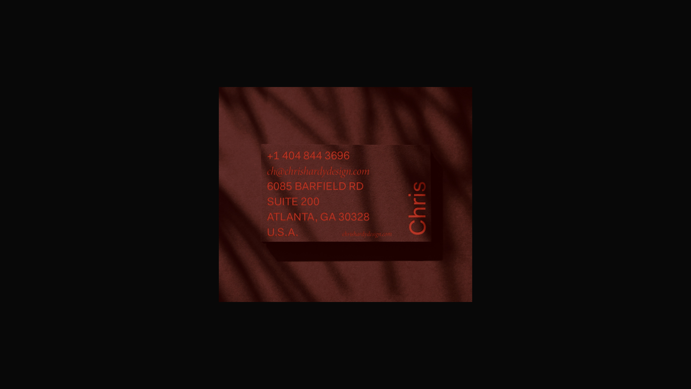Dark red business card with contact information, casting shadows on a textured dark red background.