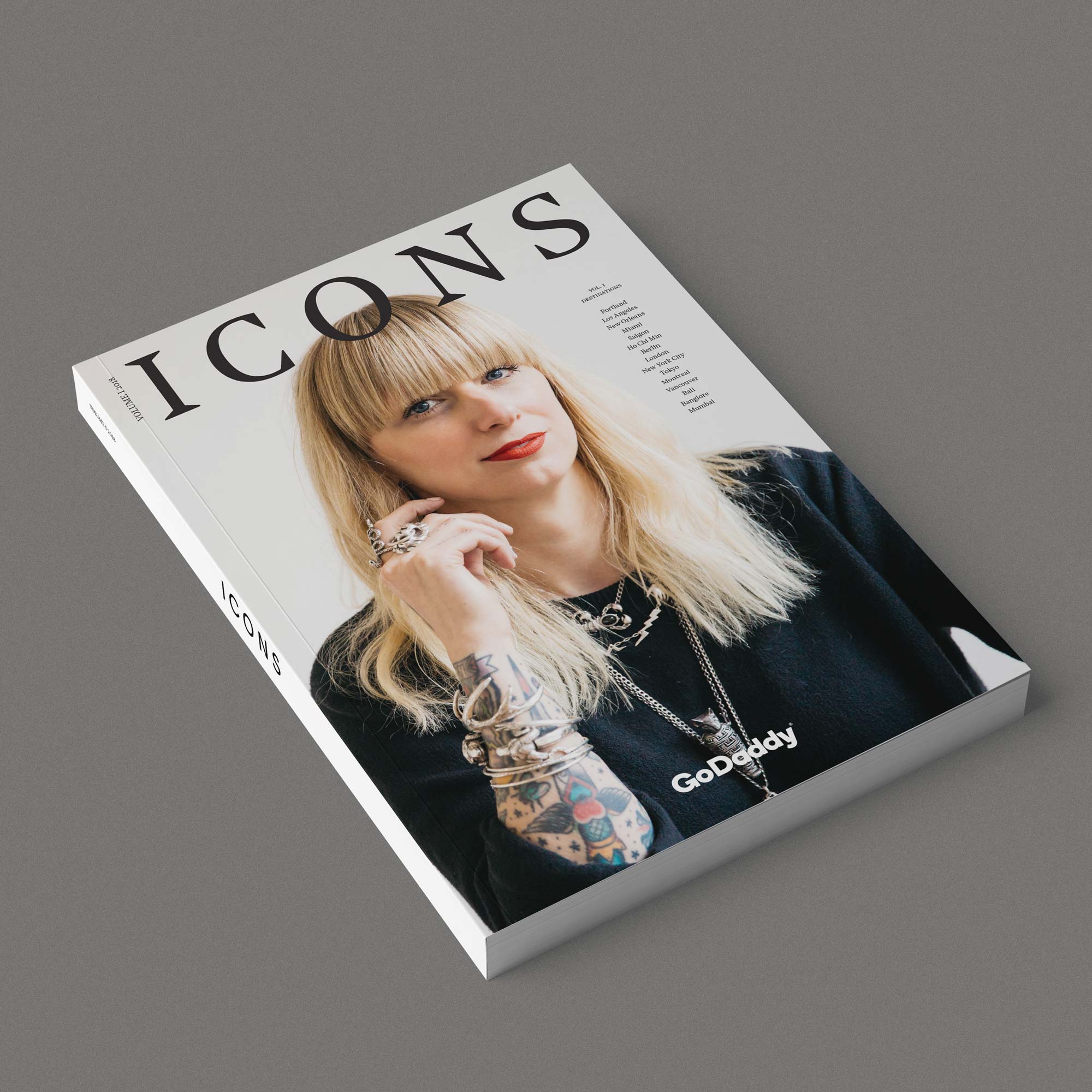 Magazine cover titled ICONS featuring a blonde woman with tattoos, multiple rings and bracelets, wearing a black top and red lipstick.