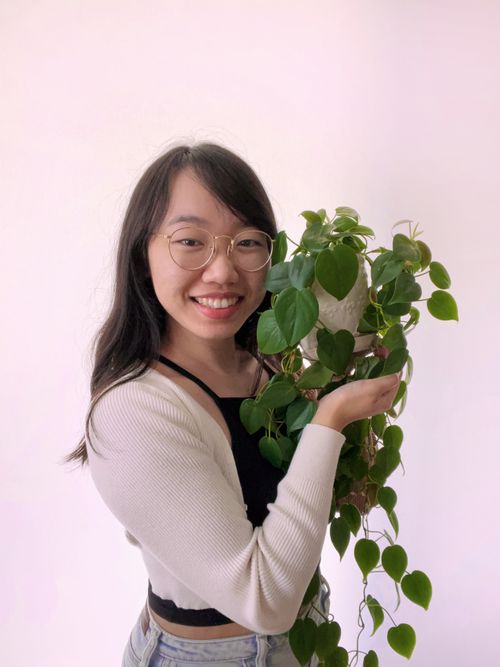 Headshot of Julie smiling, holding a plant next to her face.