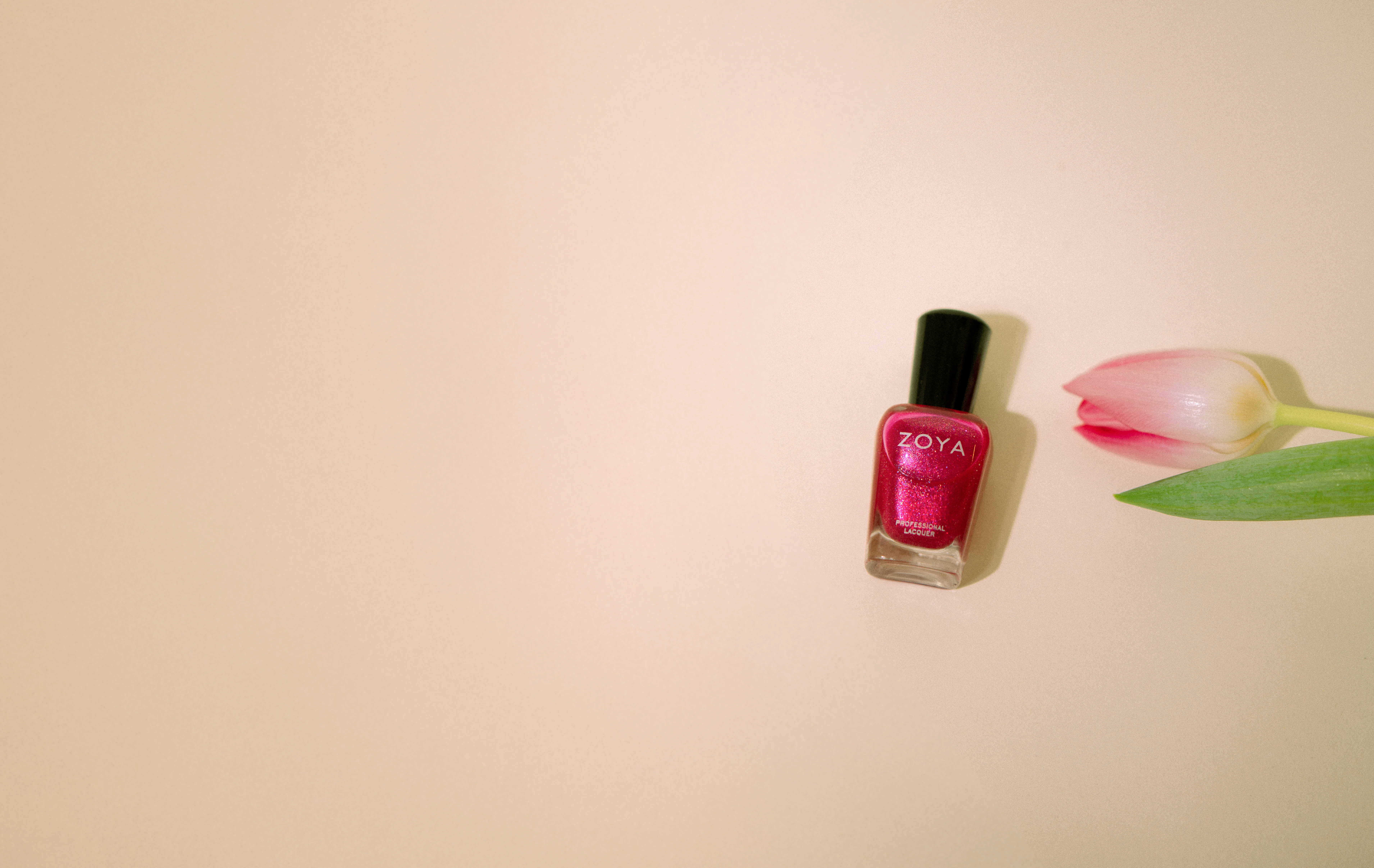 Zoya Nagellack in einem leuchtenden Pinkton wird stilvoll in verschiedenen frühlingshaften Settings präsentiert: einmal elegant gehalten in einer Hand mit frisch lackierten Nägeln, eingebettet in einen Blumenstrauß aus rosa Tulpen und weißen Blüten, und einmal minimalistisch neben einer einzelnen Tulpe auf beigem Hintergrund. Die Bilder vereinen Kosmetik, Natürlichkeit und Ästhetik – perfekt für Beauty-Content, Frühlings-Inspiration oder Produktpräsentationen rund um Maniküre und Nagelpflege.