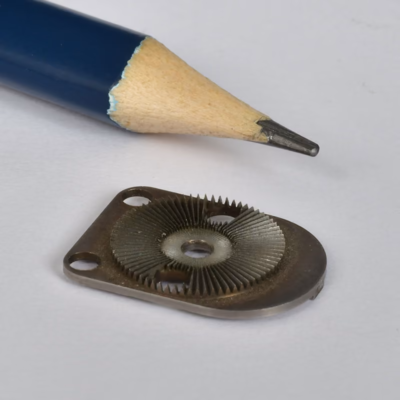 Small precision plate part next to a pencil for scale