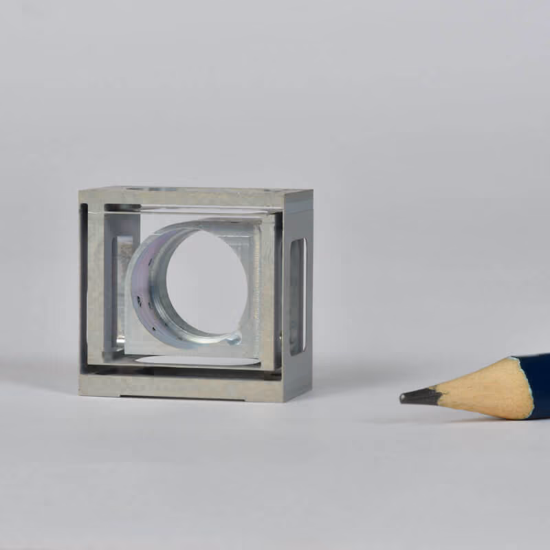 Small precision-machined block shown next to a pencil tip for scale