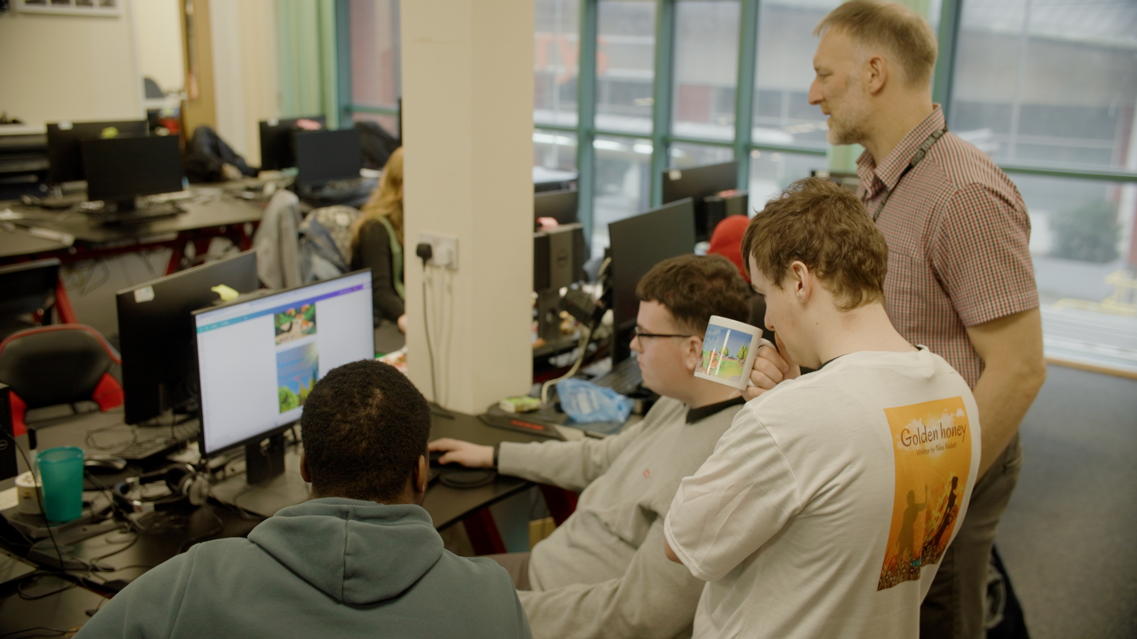 Instructor standing near students working on computer screens in a classroom