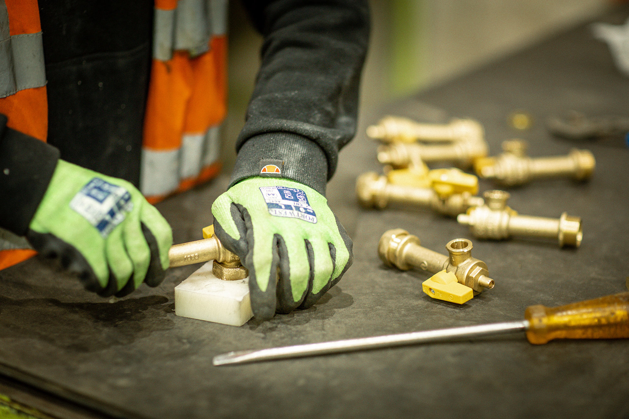 Worker wearing safety gloves assembling brass valves on a workbench